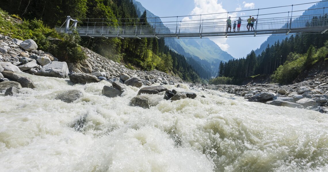 Suspension bridge over a roaring mountain stream, framed by forests and mountains. | © Holiday Region National Park Hohe Tauern
